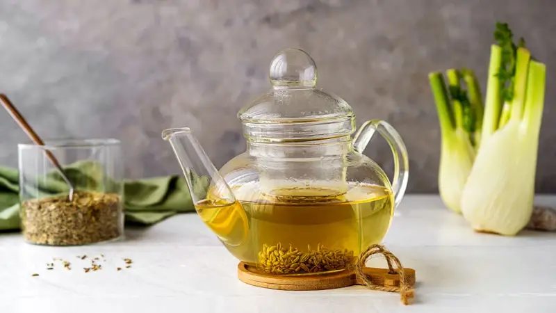 Tisana al finocchietto in teiera di vetro, con semi di finocchio e bulbi sullo sfondo. Scopri i tisana al finocchietto benefici.