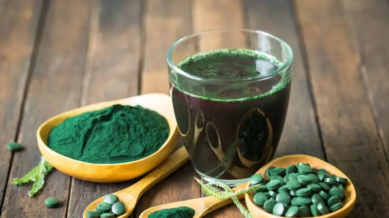 Spirulina in polvere, compresse e bevanda verde su fondo di legno. Per quanto tempo si può prendere la spirulina? Chiedi al tuo medico.